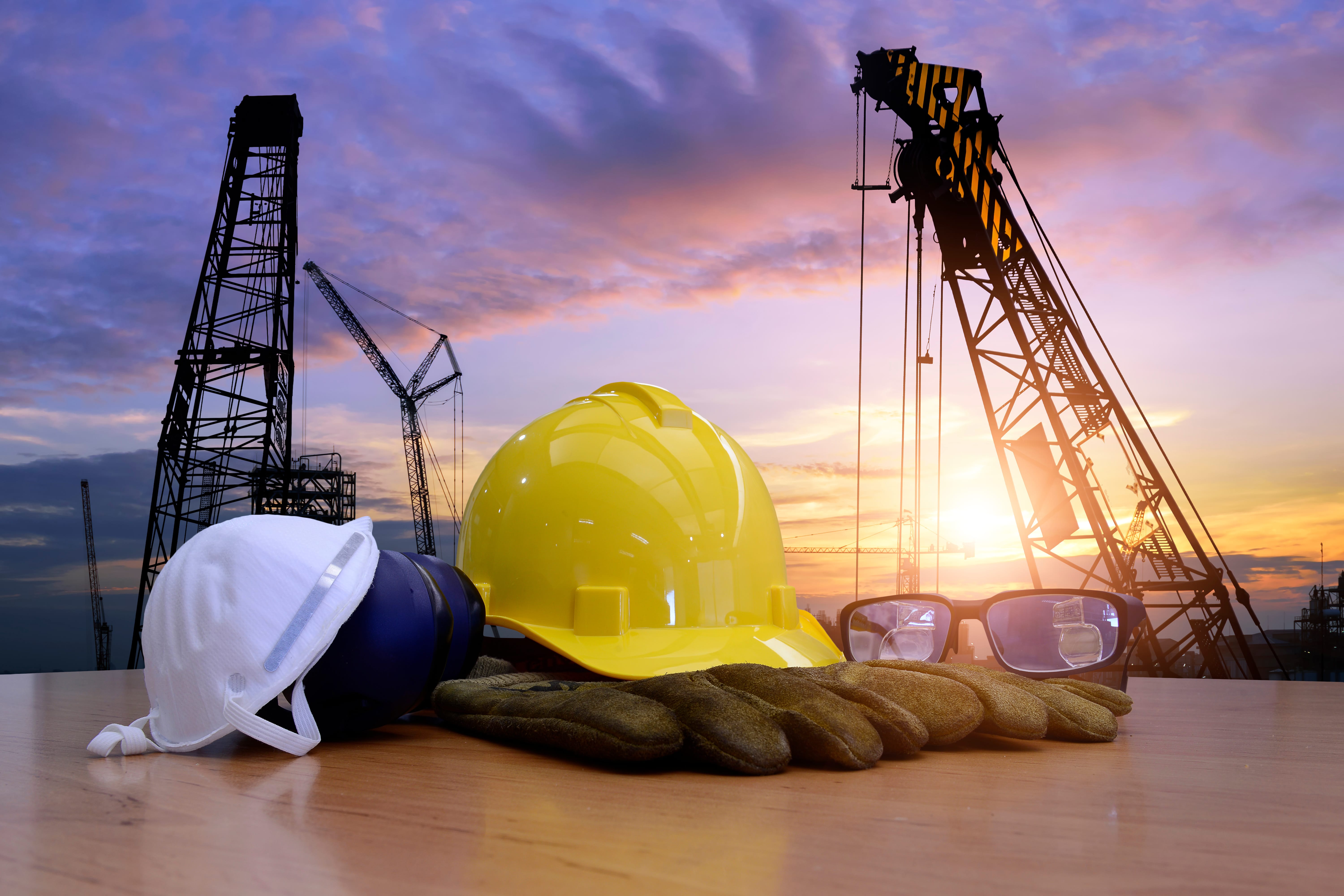 Hard hats, gloves, safety goggles + construction worksite background